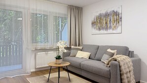 Un salon moderne avec un canapé gris, une table basse ronde en bois, une plante en pot et un grand tableau abstrait accroché au mur.