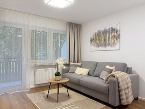 Ein modernes Wohnzimmer mit grauem Sofa, einem runden Holztisch, einer Topfpflanze und einem großen abstrakten Gemälde an der Wand.