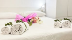 Ein ordentlich bezogenes Bett mit gerollten weißen Handtüchern und einem Blumenstrauß, der mit einem rosafarbenen Band gebunden ist.