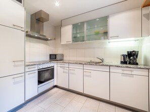 Eine moderne Küche mit weißen Schränken, einer Mikrowelle, einem Backofen, einer Kaffeemaschine und einem Vitrinenschrank.