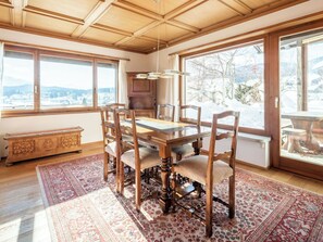 Ein Esszimmer mit Holztisch und -stühlen, großen Fenstern mit Blick auf Schnee und einem traditionellen Teppich.