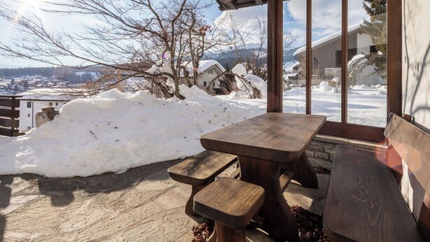 Um banco e uma mesa de madeira em frente a um edifício, com vista para uma paisagem nevada.