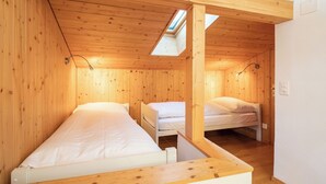 Quarto compacto com duas camas, paredes de madeira, um claraboia e teto branco.