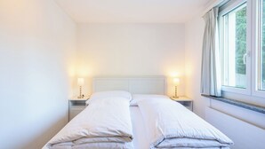 Ein Doppelbett mit weißen Bettwäsche, zwei Nachttische mit Lampen und ein Fenster mit Vorhängen.