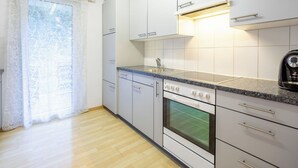 Eine moderne Küche mit weißen Schränken, einer Granit-Arbeitsplatte, einem Einbauofen und einem Fenster mit durchsichtigen Vorhängen.