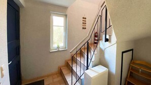 Un escalier avec une rampe en métal, une fenêtre donnant sur un paysage verdoyant et un climatiseur blanc.