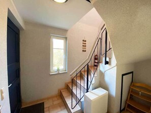 Eine Treppe mit Metallgeländer, ein Fenster mit Blick auf Grünflächen und eine weiße Klimaanlage.