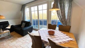 Un salon avec un canapé, une table à manger et des chaises, une lampe, et une vue sur une clôture bleue, visible à travers de grandes fenêtres.