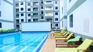 A swimming pool with lounge chairs, a pool rules sign, and a building with balconies in the background.