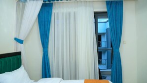 A hotel room with a bed, white curtains, blue curtains, and a balcony with a railing.