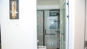 A modern bathroom with a glass shower enclosure, a toilet, and a framed artwork on the wall.
