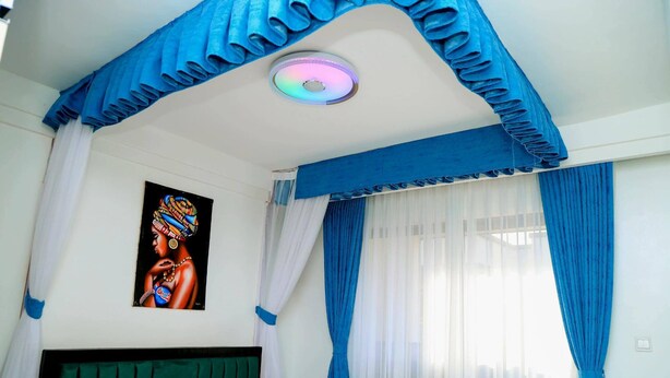 A room with a bed, a ceiling light, a painting, and blue curtains.