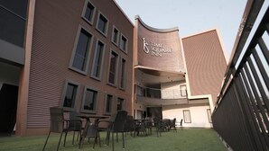 Een modern gebouw met een gebogen gevel, een bord met 'Time Square Inn', terras met stoelen en tafels, en een klein gazon.
