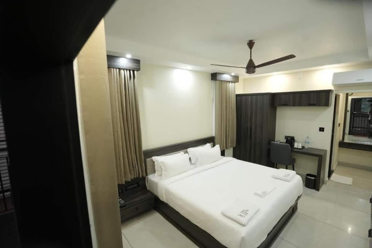 Una habitación de hotel con una cama grande, un escritorio, una silla, un ventilador de techo y un baño visible a través de una puerta abierta.