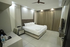 A hotel room with a bed, bedside table, desk, chair, curtains, and a ceiling fan.