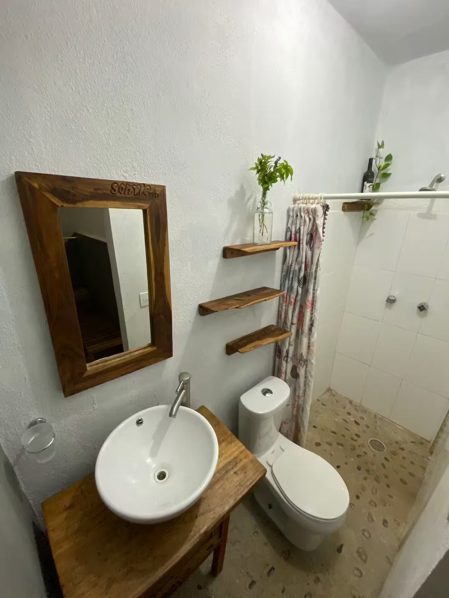 A bathroom with a wooden vanity, a white sink, a toilet, a mirror with a wooden frame, and a shower area.