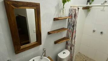 A bathroom with a wooden vanity, a white sink, a toilet, a mirror with a wooden frame, and a shower area.