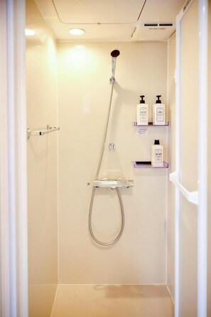 A shower with a handheld showerhead, a wall-mounted soap dispenser, and a small shelf with toiletries. - Shukusei Shibuya (Shibuya)