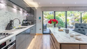 A modern kitchen with a marble countertop, stainless steel appliances, and a dining area with a view of the garden. - Luxury Jurassic Spa Retreat | Private Swim Spa, Hot Tub & Gated Grounds (co durham)