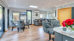 A modern living room with a dining area, grey upholstered furniture, and a large window. - Luxury Jurassic Spa Retreat | Private Swim Spa, Hot Tub & Gated Grounds (co durham)