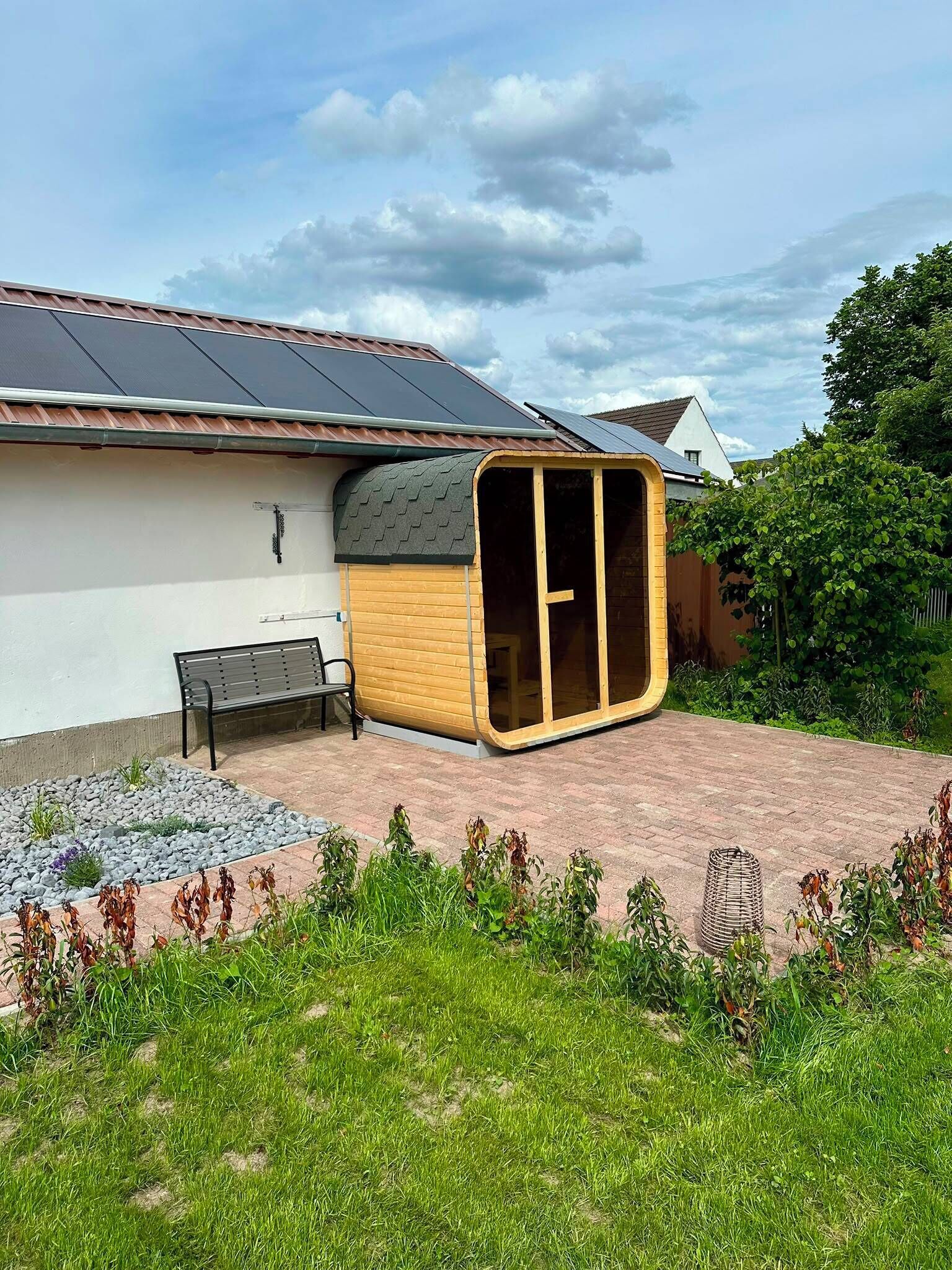 Una casa con techo de paneles solares, estructura de madera con puerta de vidrio, un banco y un jardín.