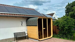 A house with a solar panel roof, a wooden structure with a glass door, a bench, and a garden area. - Liv OG Vacation Rental in Rechlin: with a garden, Wi-Fi, and private parking (Rechlin)
