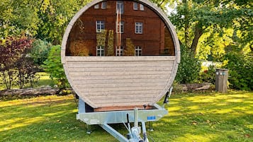 A large, cylindrical structure resembling a barrel with a metal frame, situated on a grassy area with trees and a small shed in the background.