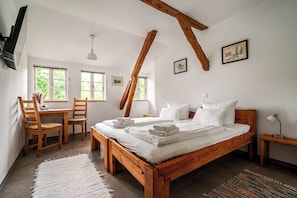A bedroom with a wooden bed, a desk with chairs, and large windows.