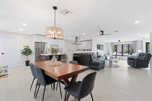 A modern kitchen with white cabinets, a dining table with chairs, and a chandelier. - 🏖️Sunshine Dock House | On Canal w/ Dock | Private Pool | Games 🏖️ (Fort Myers Beach)