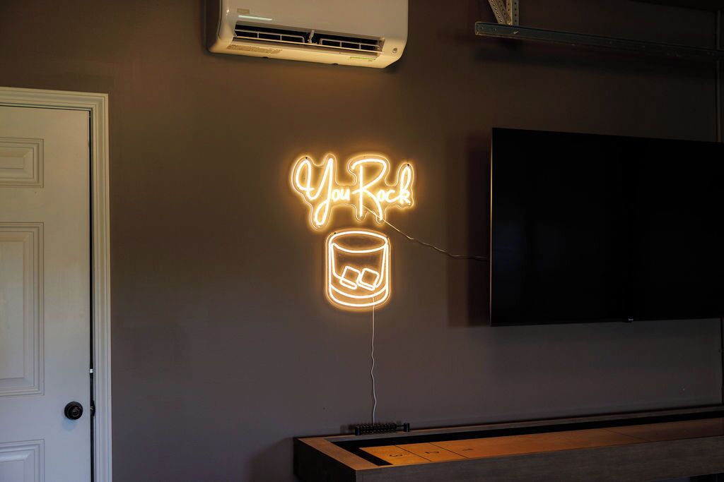 A neon sign with the text 'You Rock' and a glass icon, mounted on a wall above a flat-screen TV.