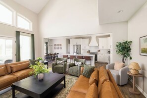 Ein geräumiger Wohnbereich mit einer Couch, Sesseln und einem Couchtisch. Im Hintergrund ist eine Küche mit weißen Schränken und einem Essbereich zu sehen.
