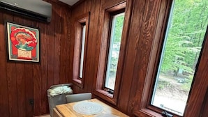 Zona pranzo con tavolo e sedie in legno, ampie finestre vista su spazi verdi e condizionatore d'aria a parete.