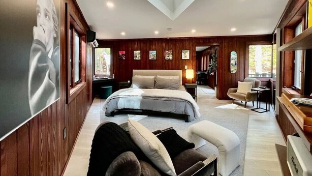 Un'ampia camera da letto con un letto grande, un'area salotto con divano e poltrone, pannelli in legno e opere d'arte alle pareti.