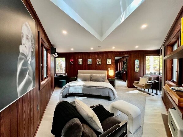 A spacious bedroom with a large bed, a seating area with a sofa and armchairs, wooden paneling, and artwork on the walls. - Ridgeline Treehouse at Cherryfield Luxury Camping (Brevard)