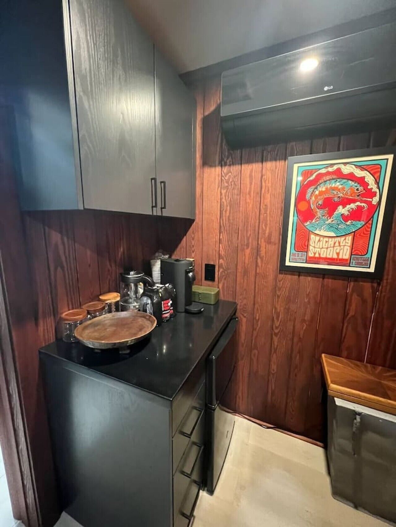 A compact kitchen with wooden cabinets, a black countertop, and a framed poster on the wall.