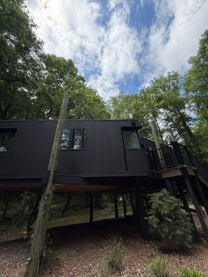 A modern black cabin elevated on stilts in a forest. - Ridgeline Treehouse at Cherryfield Luxury Camping (Brevard)