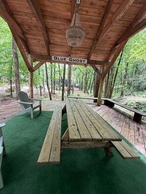 A wooden pavilion with a picnic table and chairs, surrounded by a forest. - Blueghost Treehouse at Cherryfield Luxury Camping (Brevard)