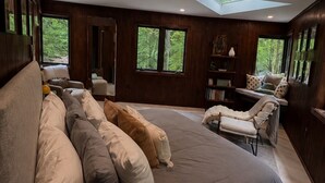 A bedroom with a large bed, a skylight, a window, and a reading area with a chair and books. - Blueghost Treehouse at Cherryfield Luxury Camping (Brevard)