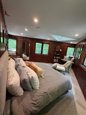 A spacious bedroom with a large bed, a sitting area with a chair, and a skylight. - Blueghost Treehouse at Cherryfield Luxury Camping (Brevard)