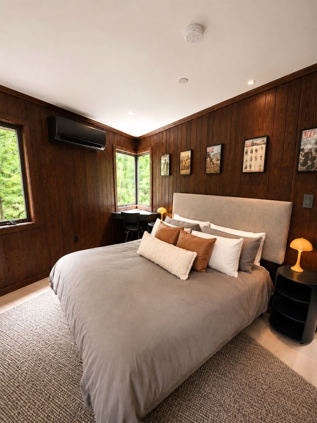 A bedroom with a large bed, wooden walls, a desk, and a window.