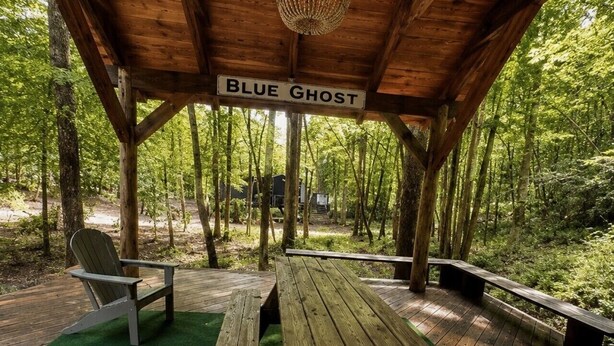 A covered wooden deck with a bench and picnic table, surrounded by trees. - Blueghost Treehouse at Cherryfield Luxury Camping (Brevard)