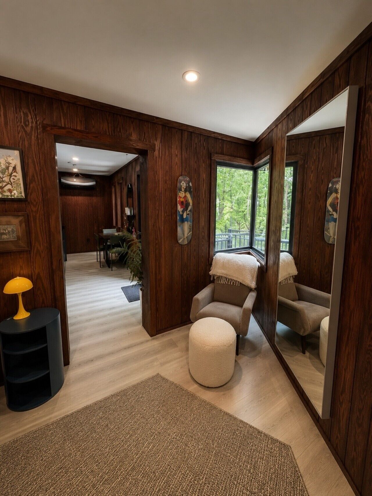 A spacious room with a large mirror, a round ottoman, and a seating area with a chair and a sofa.