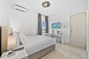 A hotel room with a bed, bedside table with a lamp, a desk with a chair, a television, and an air conditioning unit. - Modern 3BR Villa w/ Pool & Cabana, Oranjestad (Oranjestad)
