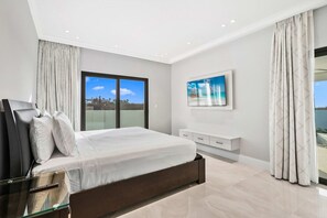 A modern bedroom with a large bed, a glass door leading to a balcony, a white bedside table, and a painting on the wall. - Modern 4BR Pool Villa w/ Lighthouse View, Arashi (Noord)