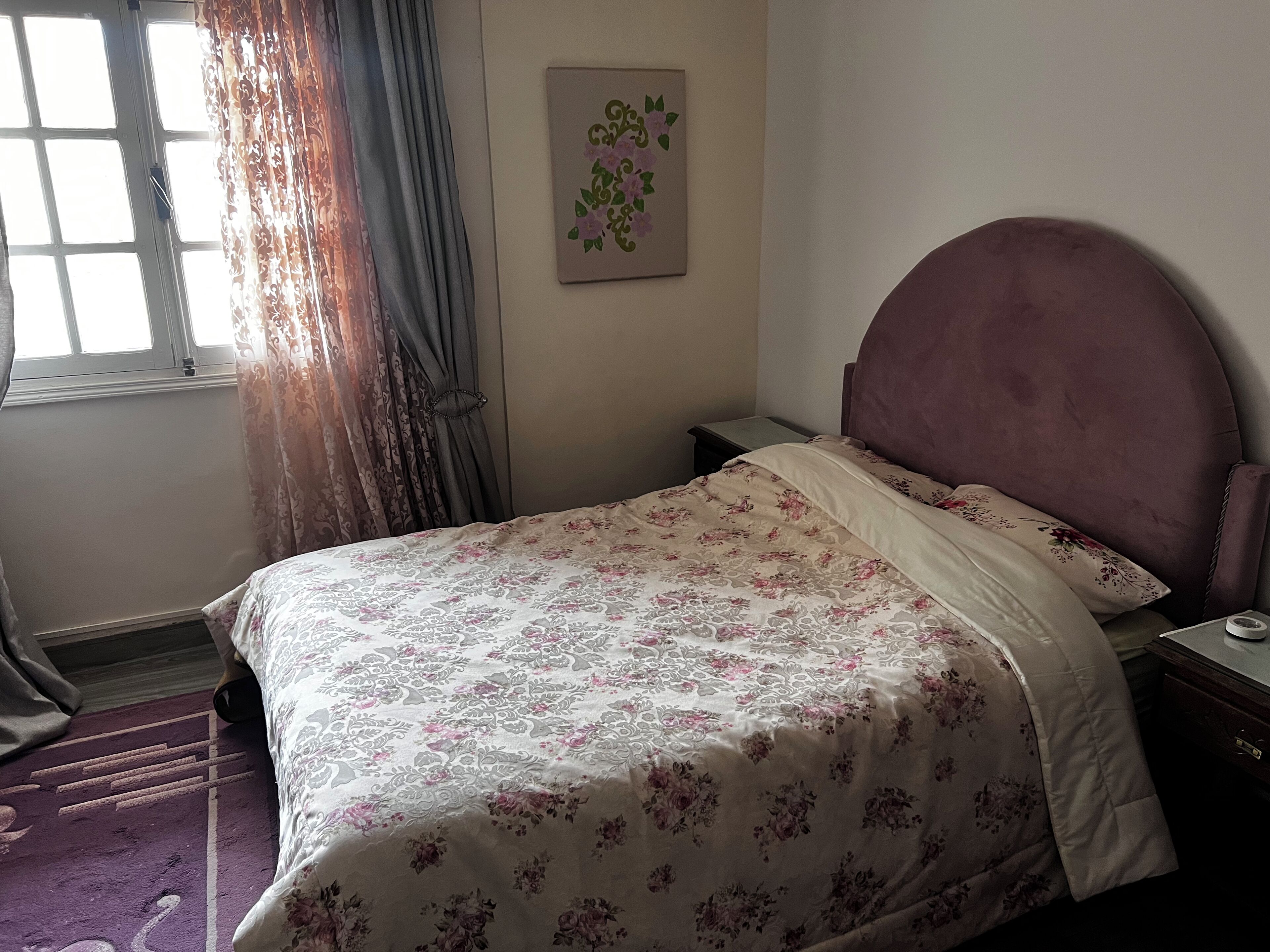 Une chambre à coucher avec un lit, une table de chevet, une horloge murale et une fenêtre avec des rideaux.