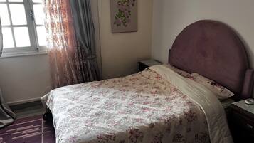 Une chambre à coucher avec un lit, une table de chevet, une horloge murale et une fenêtre avec des rideaux.
