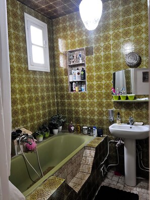 Ein Badezimmer mit einer grünen Badewanne, einem weißen Waschbecken und gemusterten Fliesen.