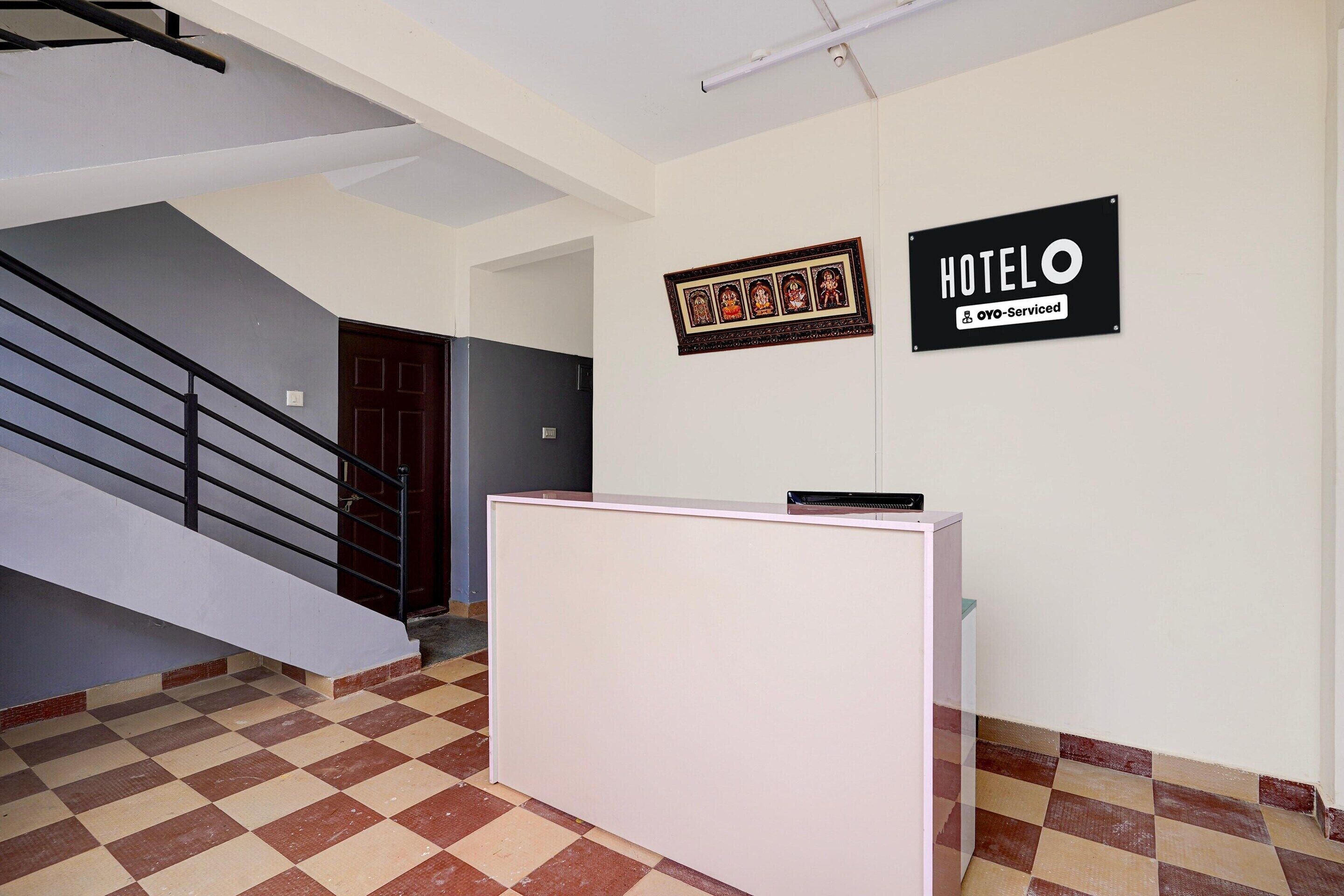Un mostrador de recepción, una escalera y dos carteles que indican 'HOTEL' y 'OYO-Serviced' en un edificio.
