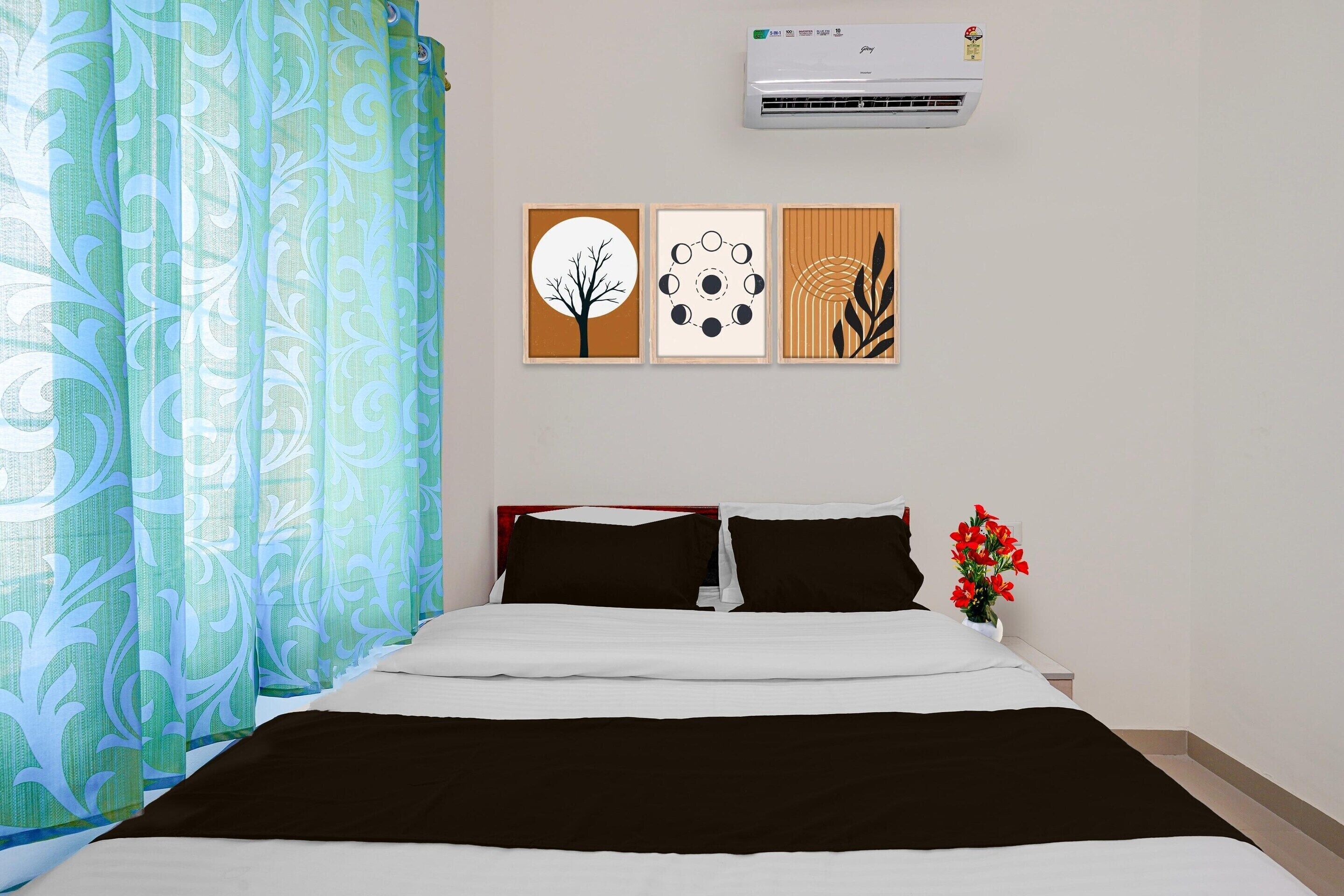 A hotel room with a bed, air conditioning unit, and three framed artworks on the wall.