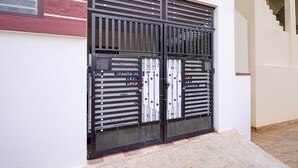 A black metal gate with a mesh screen, attached to a white wall with a red brick pattern above it. - Classic Seven Hills (Bengaluru)